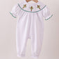 White baby romper with embroidered details on a wooden hanger against a beige background